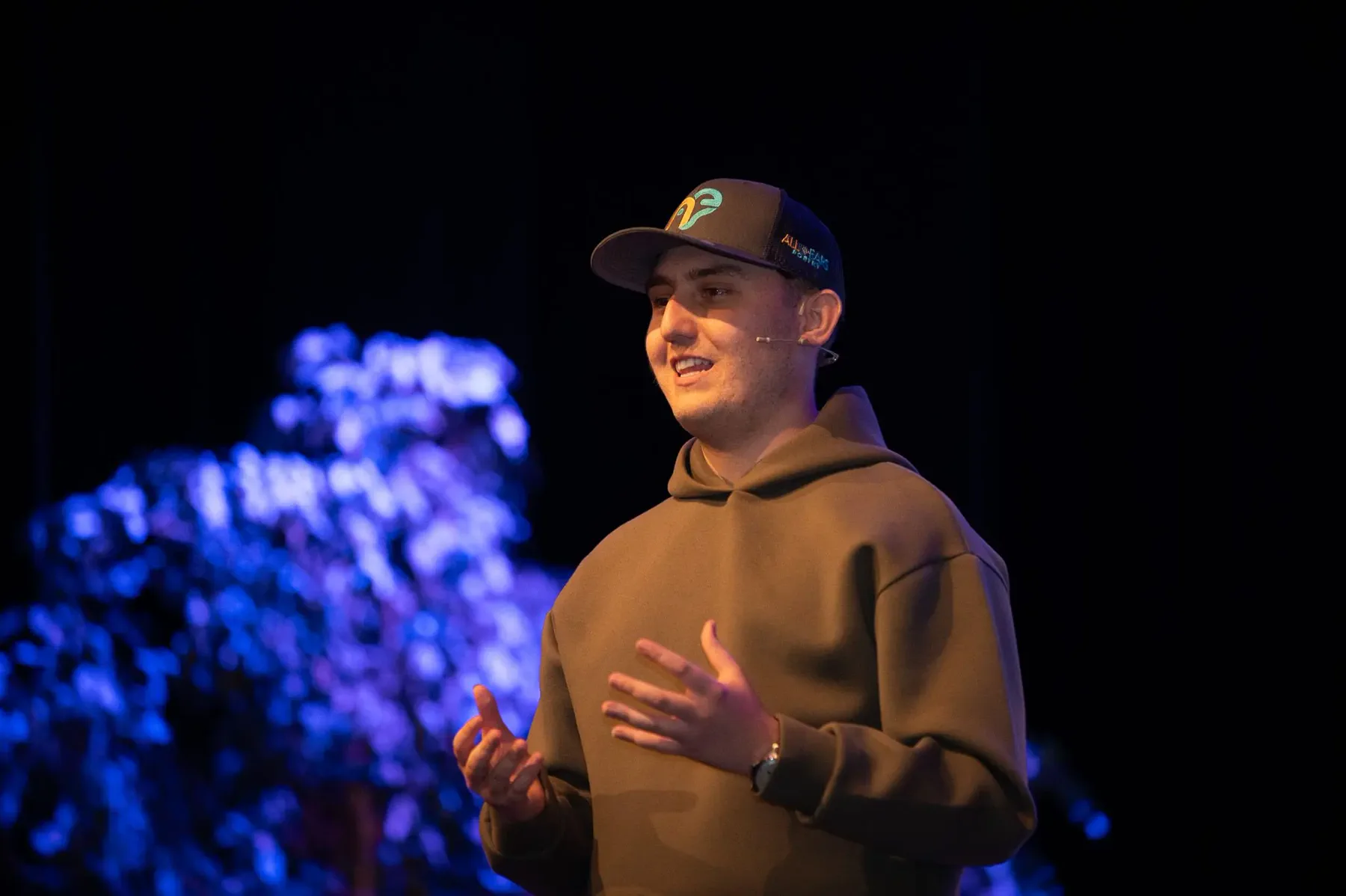 Joseph Roberts speaking on stage wearing a cap and headset microphone