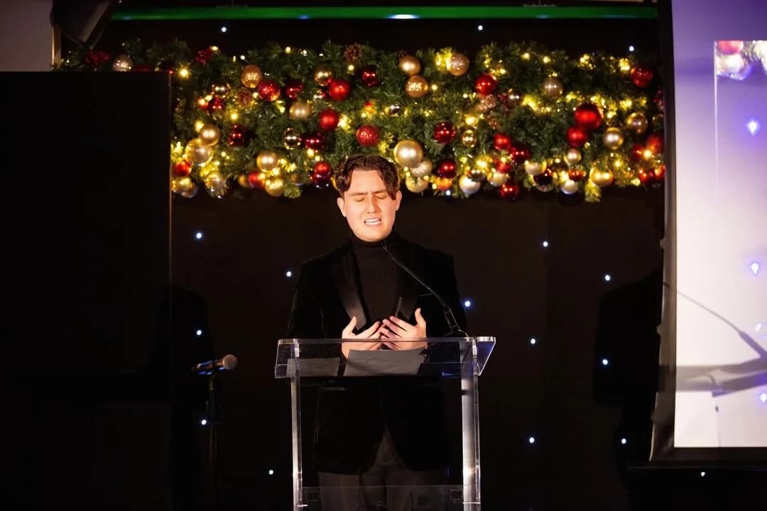 Joseph Roberts performing at a lectern with festive decorations behind him