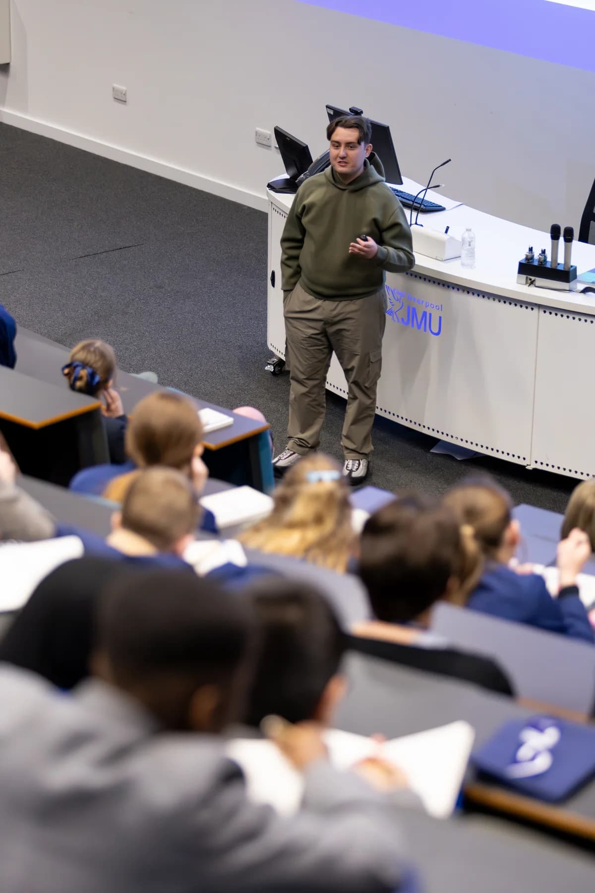 Joseph Roberts addressing students in a lecture theatre with Liverpool JMU branding